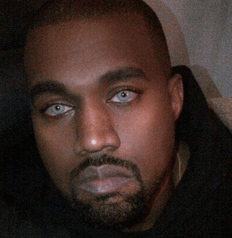 kanye west is wearing a black hoodie and has a beard and blue eyes .