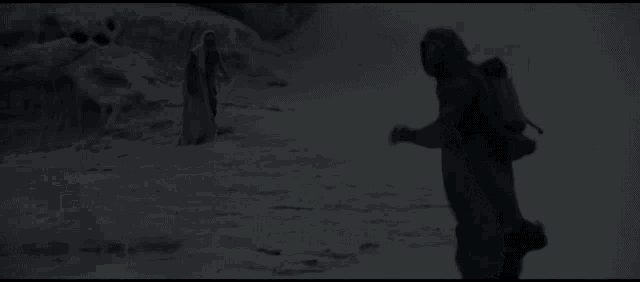 a couple of people are standing in front of a large black object in the desert .