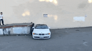 a white car is parked in a parking lot next to a skateboarder