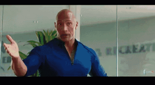 a bald man in a blue shirt is standing in front of a glass wall and making a funny face .