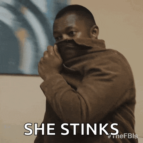 a man in a brown jacket covering his face with his jacket and the words she stinks