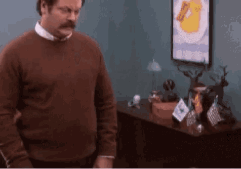 a man with a mustache is standing in a room in front of a table .
