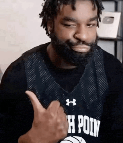 a man with a beard is giving a thumbs up sign while wearing a basketball jersey .