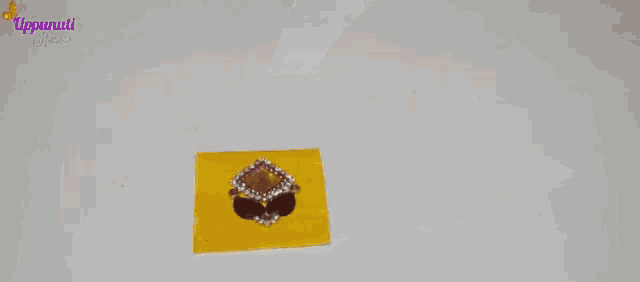 a woman 's hand is holding a yellow piece of paper with a rhinestone on it .