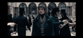 a man in a green coat and top hat is standing in a room surrounded by other men .