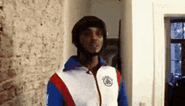 a man wearing a helmet and a jacket is standing in front of a brick wall in a room .