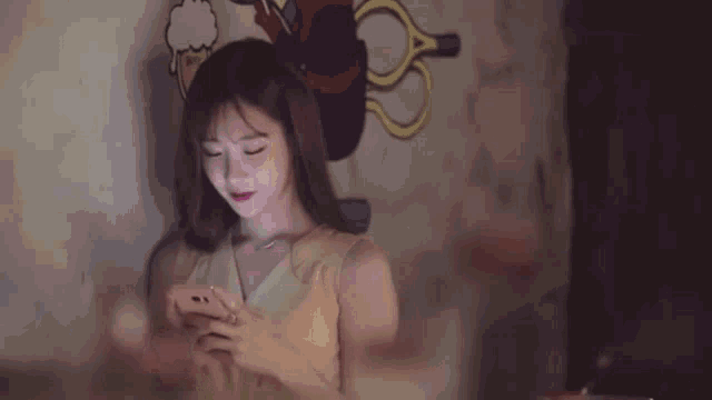 a woman is sitting in front of a wall with a cartoon on it looking at her phone .