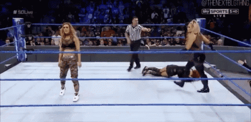 two women are wrestling in a wrestling ring with a referee in the background .