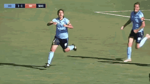 two female soccer players are running on a field with a scoreboard that says syd 1-1