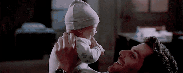 a man is holding a baby in his arms and the baby is wearing a hat .