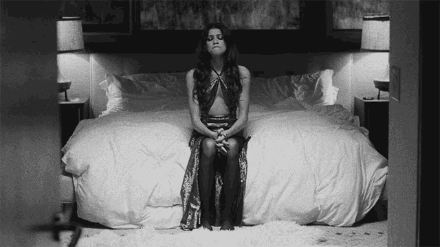 a black and white photo of a woman sitting on a bed .