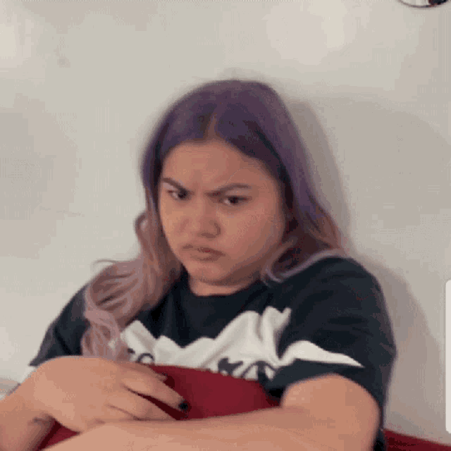 a woman with purple hair is making a funny face while holding a red pillow .