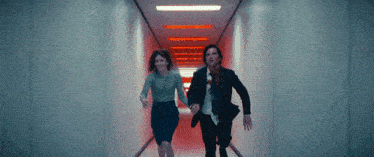 a man and a woman are running down a dark hallway holding hands