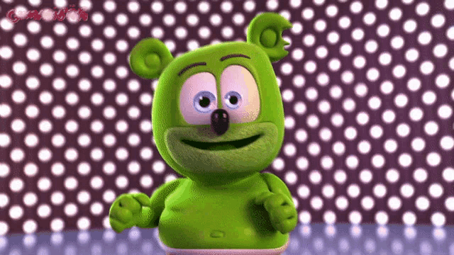 a green gummy bear is standing in front of a polka dot wall