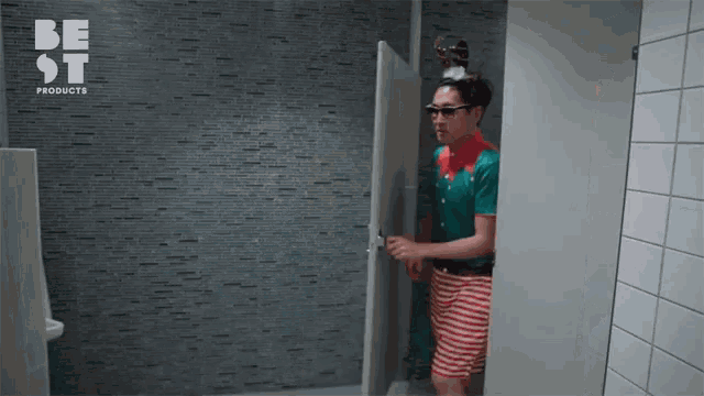 a man wearing a reindeer headband and sunglasses stands in a public restroom with a be st products logo on the wall