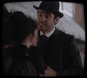 a man in a suit and hat stands next to a woman