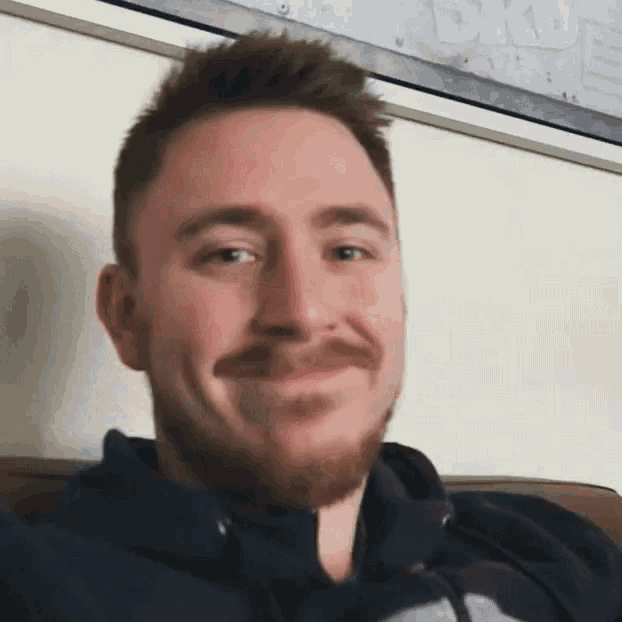 a man with a beard and mustache is sitting on a couch smiling .