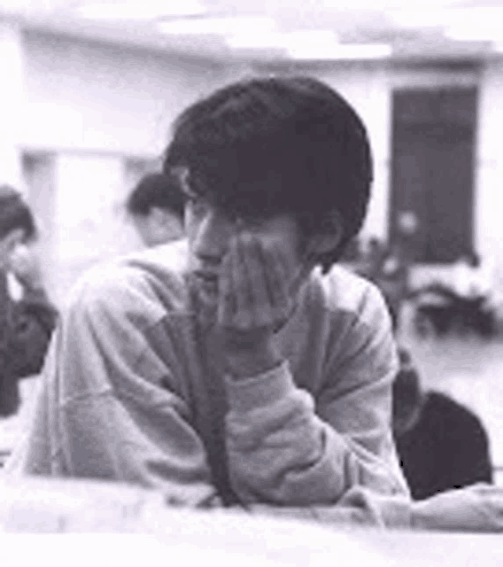 a man is sitting at a table with his hand on his face .