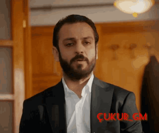 a man with a beard is wearing a suit and a white shirt with the word çukur on the bottom right