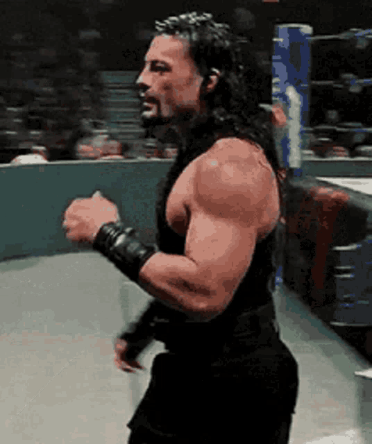 a man with long hair and a beard is standing in a ring with his fist in the air .