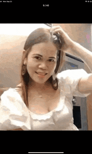 a woman in a white top is smiling and holding her hair ..