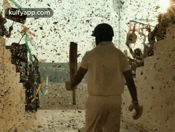 a man is holding a cricket bat and walking through a tunnel filled with confetti .