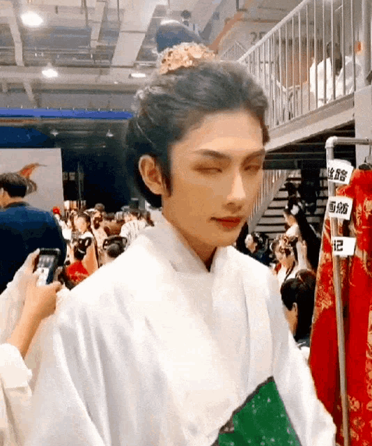 a man wearing a white robe and a flower in his hair is standing in a room with people .