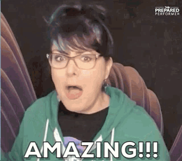 a woman wearing glasses and a green hoodie is making a surprised face and saying `` amazing '' .