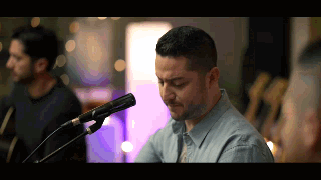 a man singing into a microphone while another man plays drums in the background