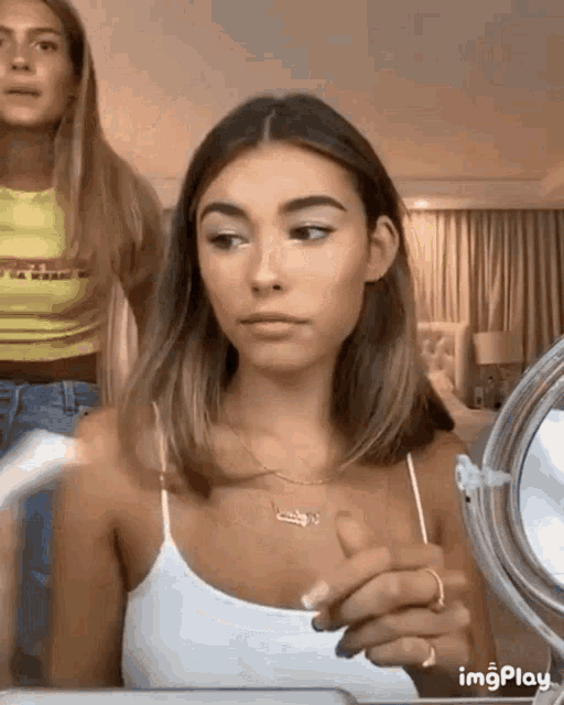 a woman in a white tank top looks at herself in the mirror