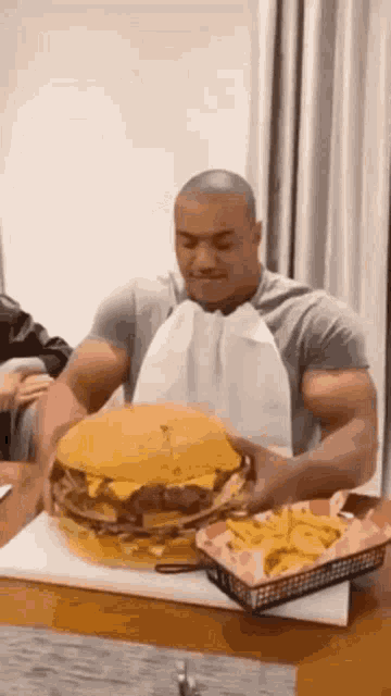 a muscular man is eating a very large hamburger and french fries .
