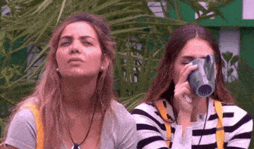 two women sitting next to each other with one drinking from a mug that says ' coca-cola ' on it