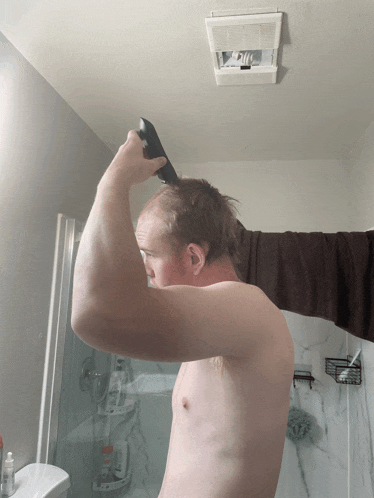 a shirtless man shaves his head in a bathroom