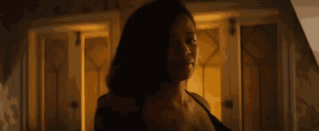 a woman in a black top is standing in a dark room in front of a door .