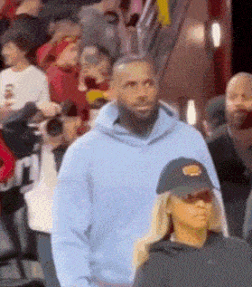 a man in a blue hoodie and a black hat is standing in front of a crowd .