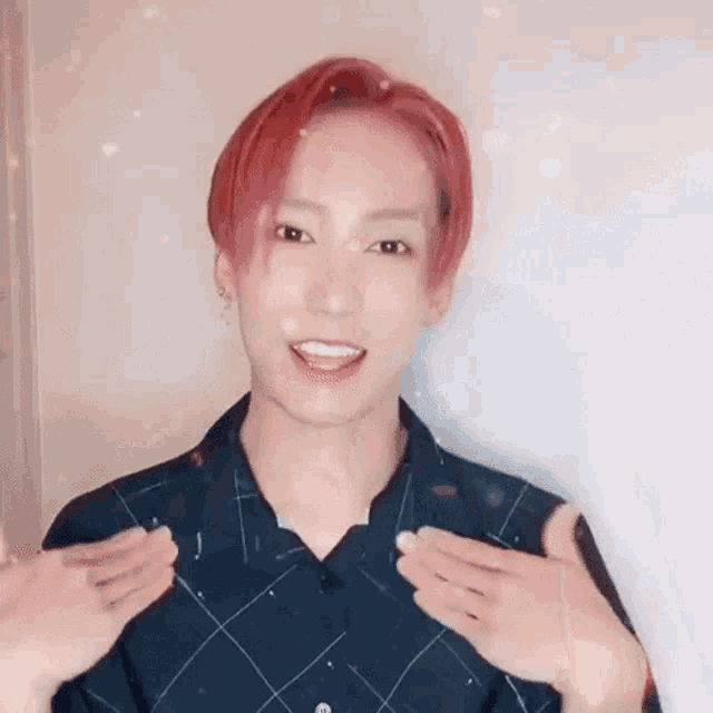 a young man with red hair is giving a thumbs up while wearing a plaid shirt .