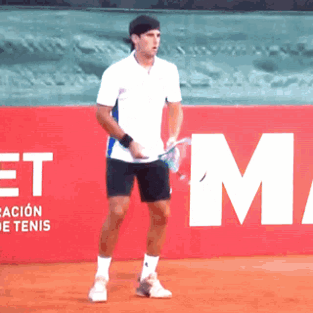 a man holding a tennis racquet in front of a red wall that says " et "