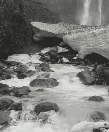 a black and white photo of a river flowing through a cave surrounded by rocks .