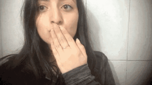 a woman is covering her mouth with her hand while wearing a ring on her finger .
