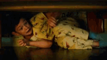 a young boy in yellow pajamas is laying under a table