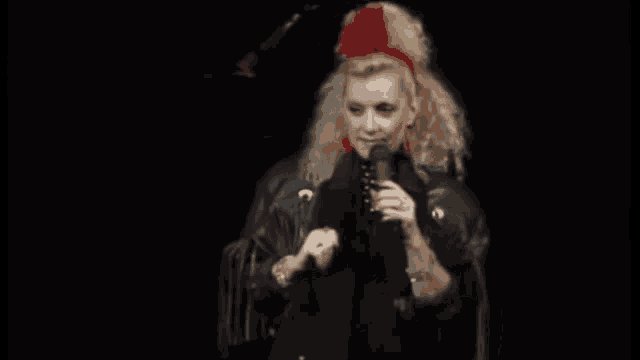 a woman wearing a red headband and a black jacket is singing into a microphone