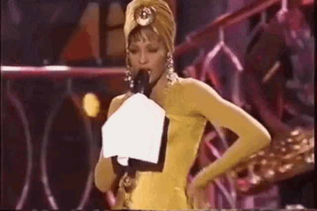 a woman in a yellow dress and turban is holding a microphone .