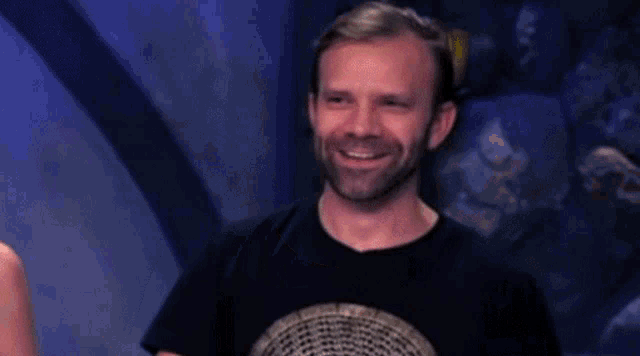 a man with a beard and a ring on his finger is waving his hand in front of a woman .