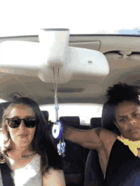 two women are sitting in a car with a rear view mirror hanging from the roof .