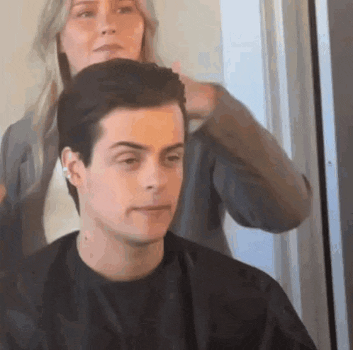 a woman is cutting a man 's hair at a salon .