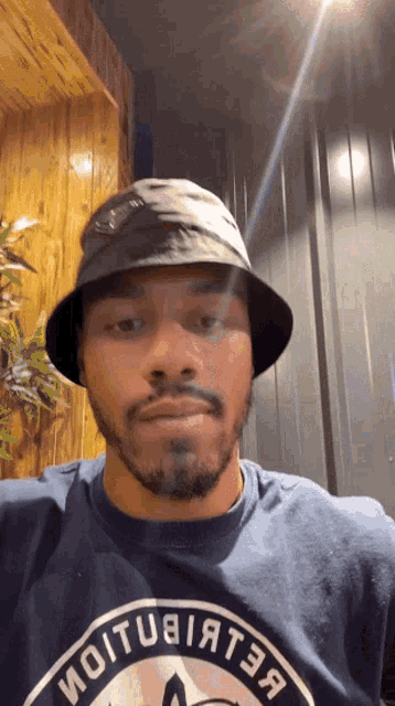 a man wearing a bucket hat and a shirt that says ioitub1at3a looks at the camera