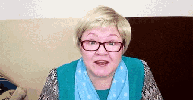 a woman wearing glasses and a blue scarf is sitting on a couch and talking .