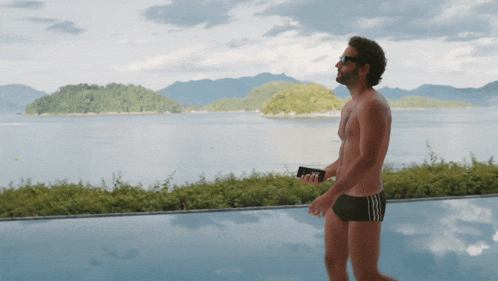 a shirtless man standing next to a swimming pool holding a wallet that says ' no ' on it