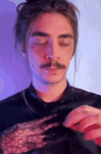 a man with long hair and a mustache is wearing a black shirt with a lace top .