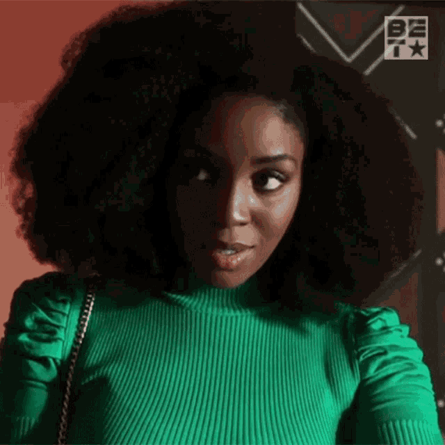 a woman in a green sweater is looking at the camera with a be a star logo in the background